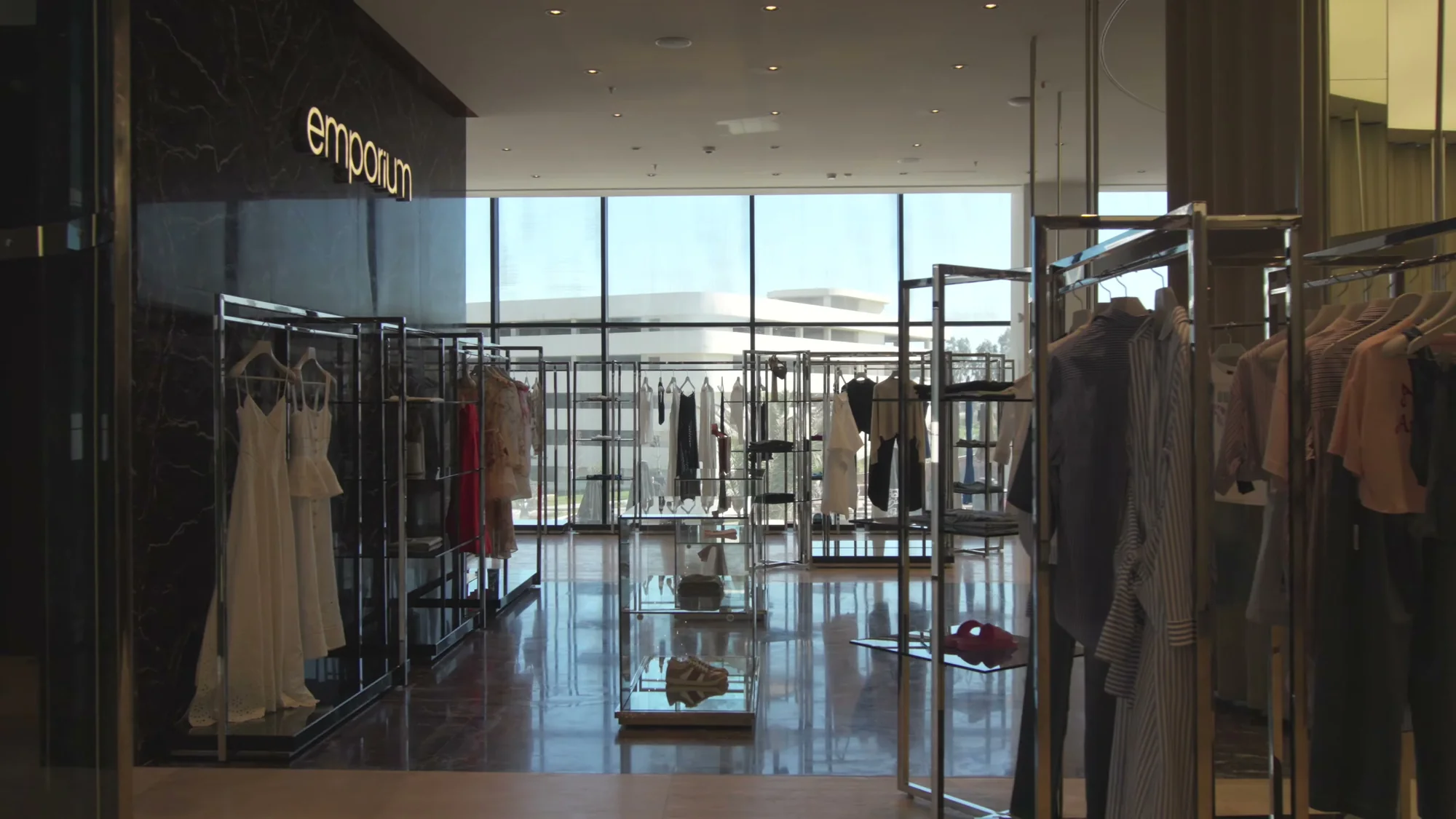 Вход в Emporium из галереи Lighthouse Mall: мраморная стена с логотипом, вешала с платьями, витражи во всю стену